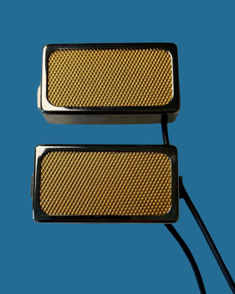 Two rectangular metallic guitar pickups with gold textured surface on a white background